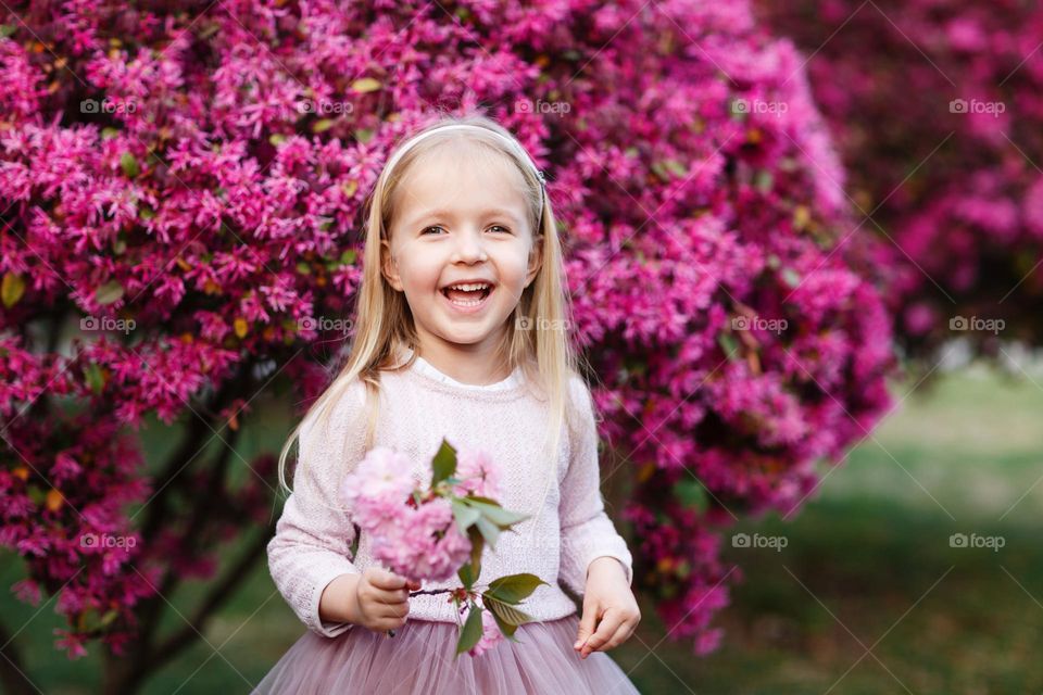 Cute little girl smiling near pink blooming tree