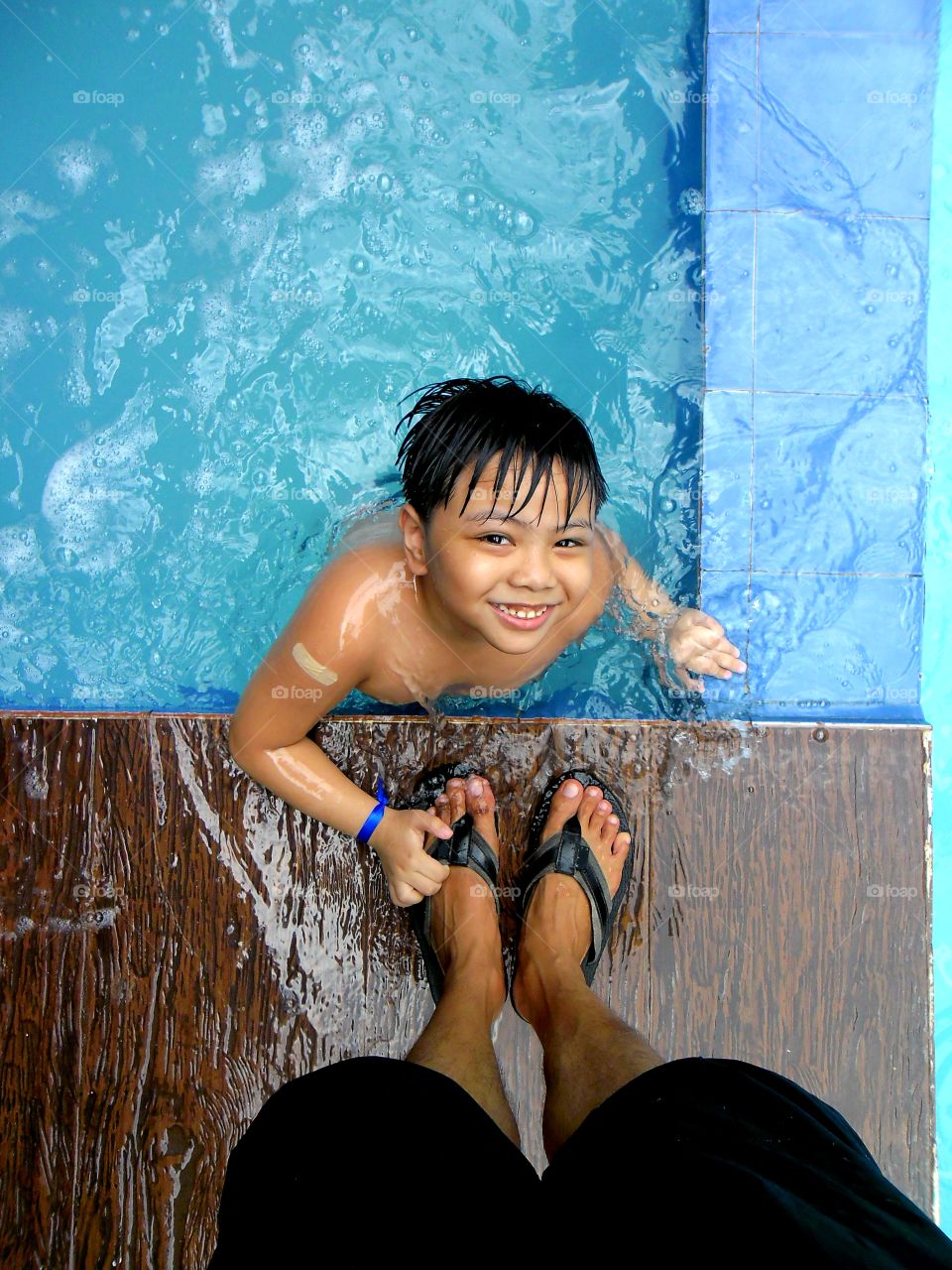 young boy in a swimming pool and an adult's feet