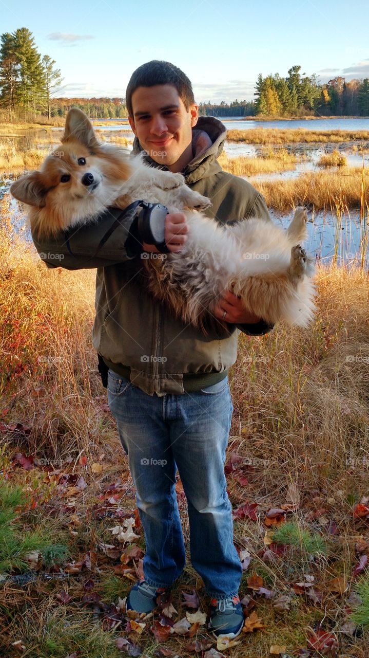 Young man carrying cute dog at lake side