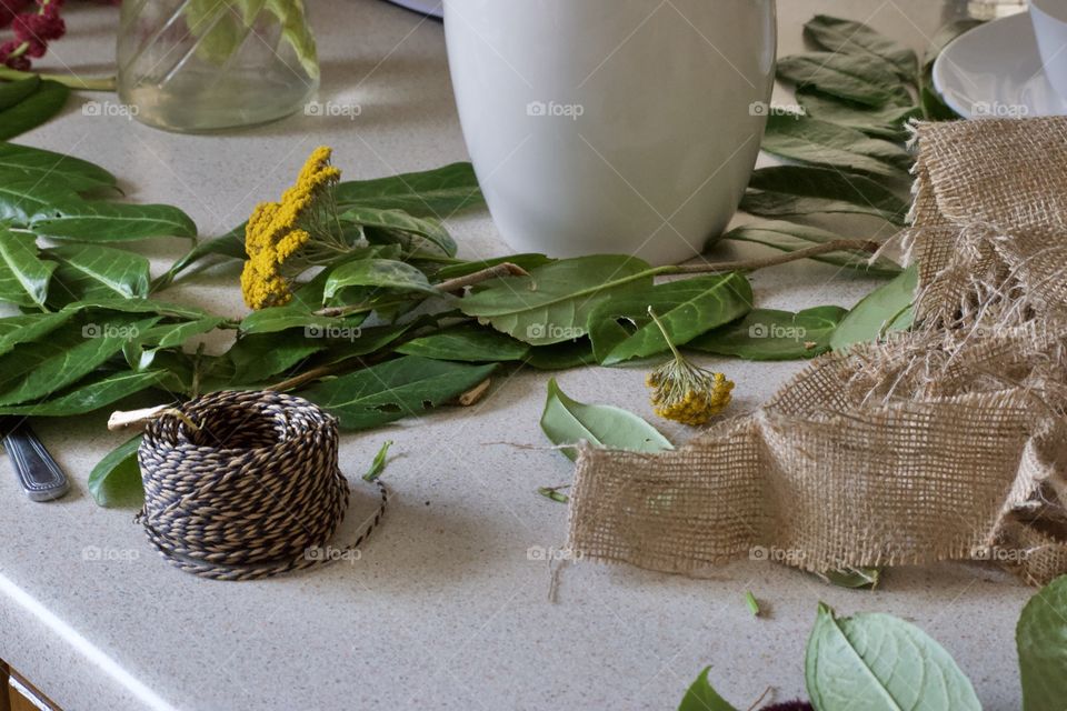 Laurel leaves and yellow flowers on a table beside a vase and hessian/burlap.