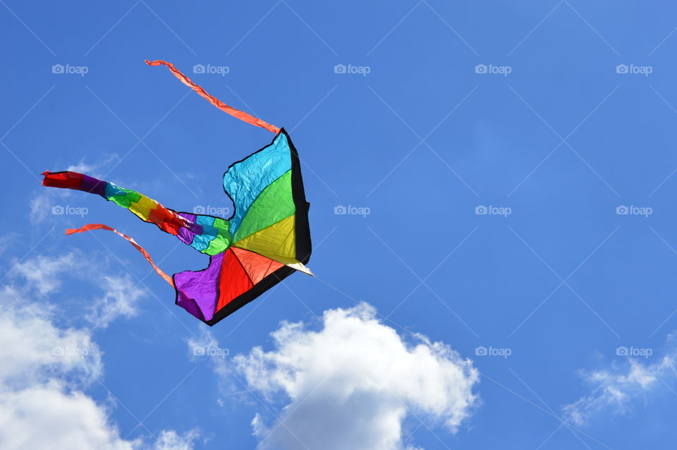 Rainbow colored kite flying in the bright blue sky 