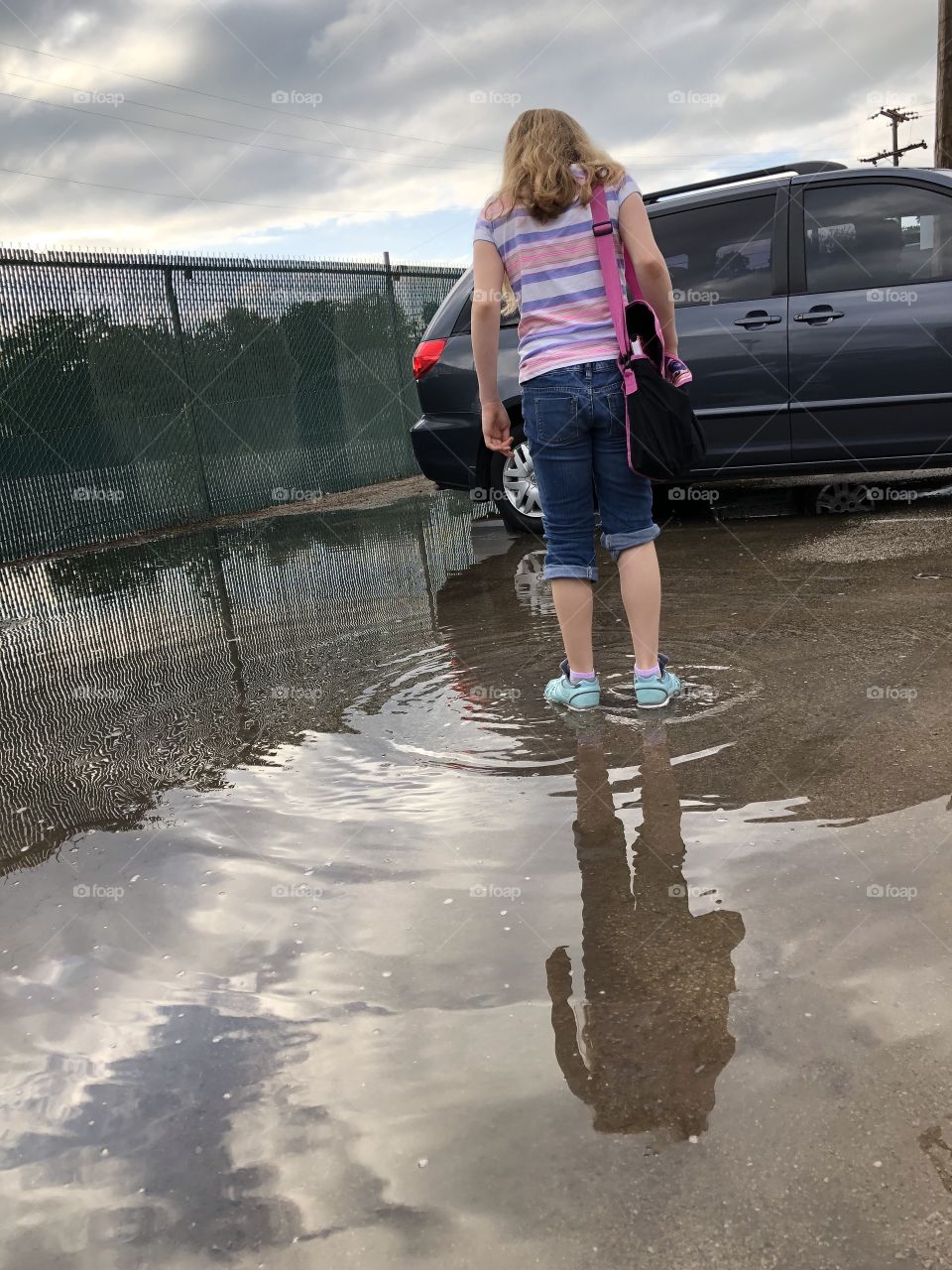 Girl in blue shoes is reflected in puddle as she wades in water with jeans rolled up
