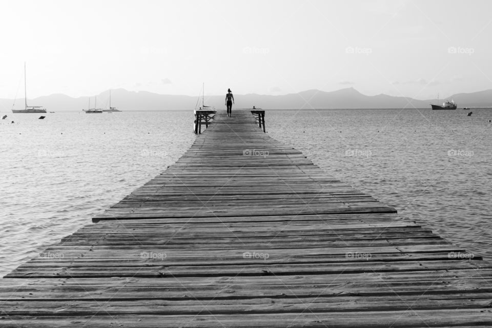 Woman walking on wooden pier in early morning, B&W