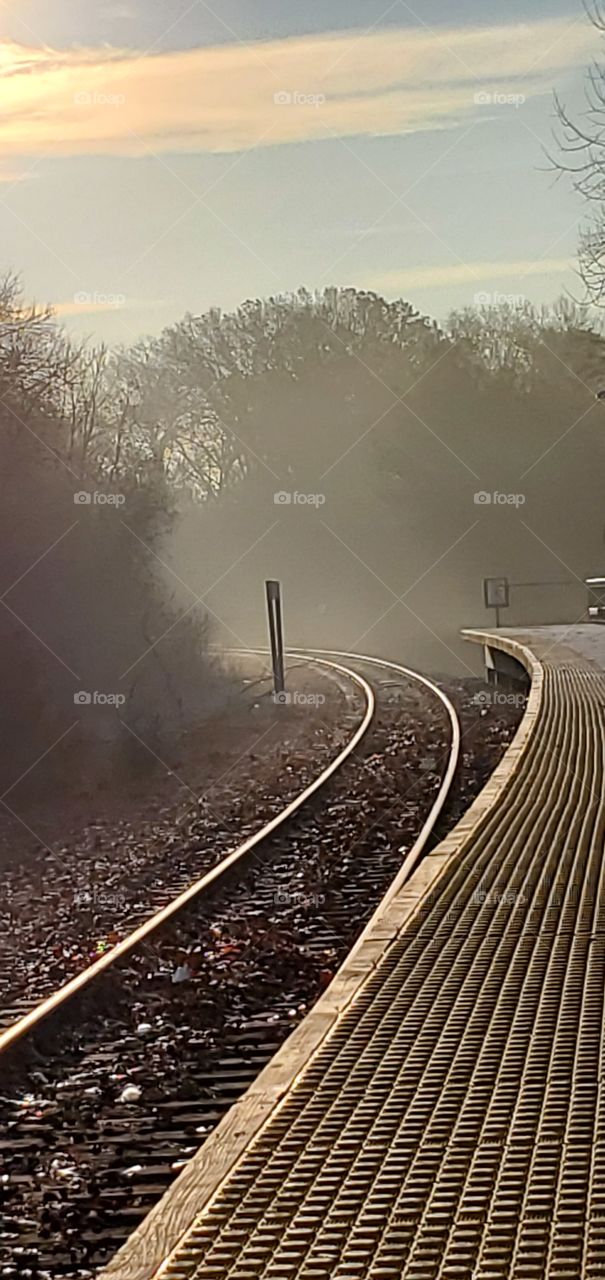 Morning haze & fog, on tracks disappearing around the corner of the commuter rail service to several stops before ending in Boston.