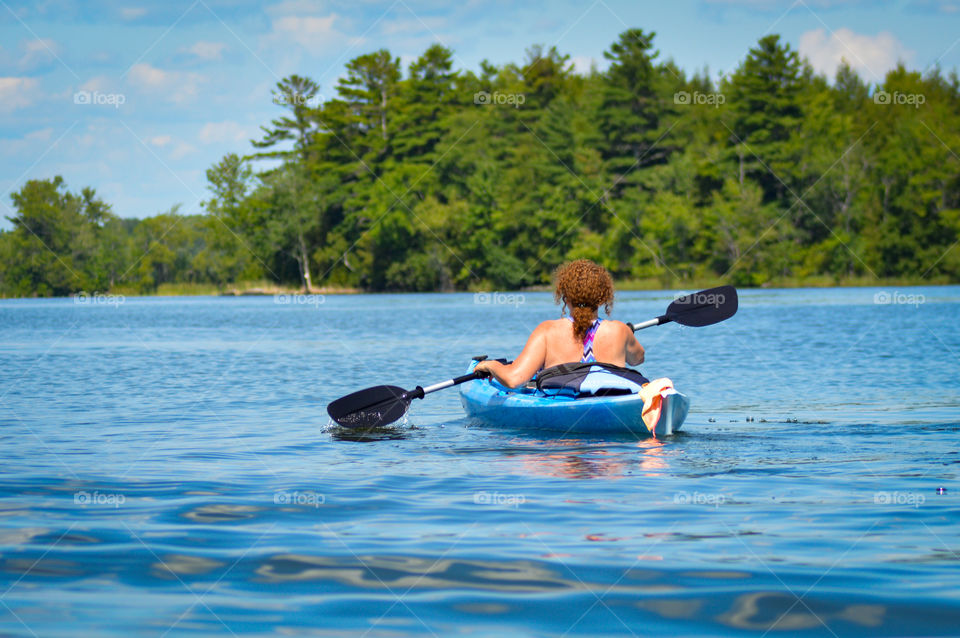 woman paddling in a blue kayak on a Maine lake during summer.