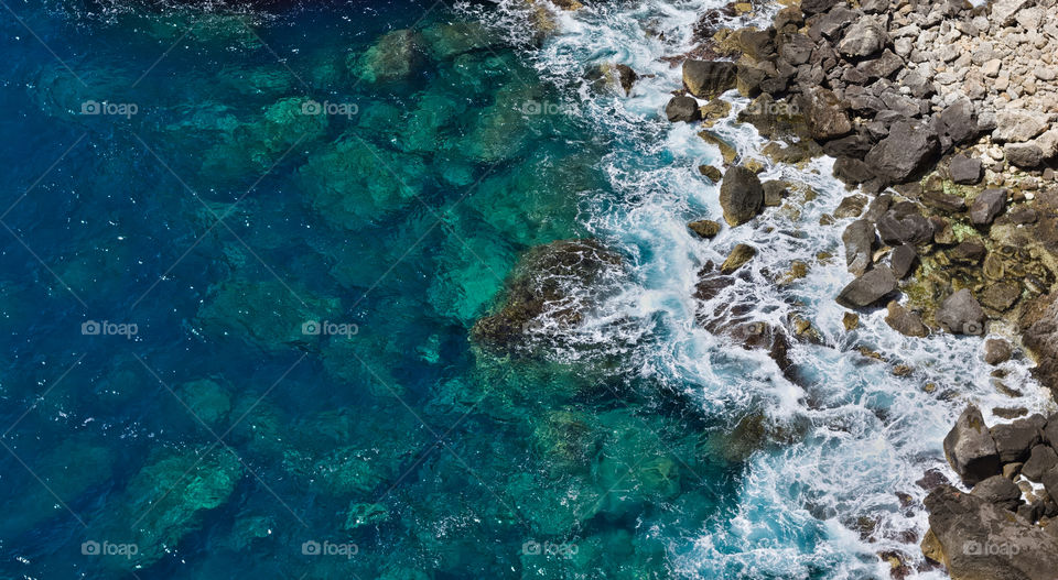 Turquoise blue waves crashing on rocky beach.