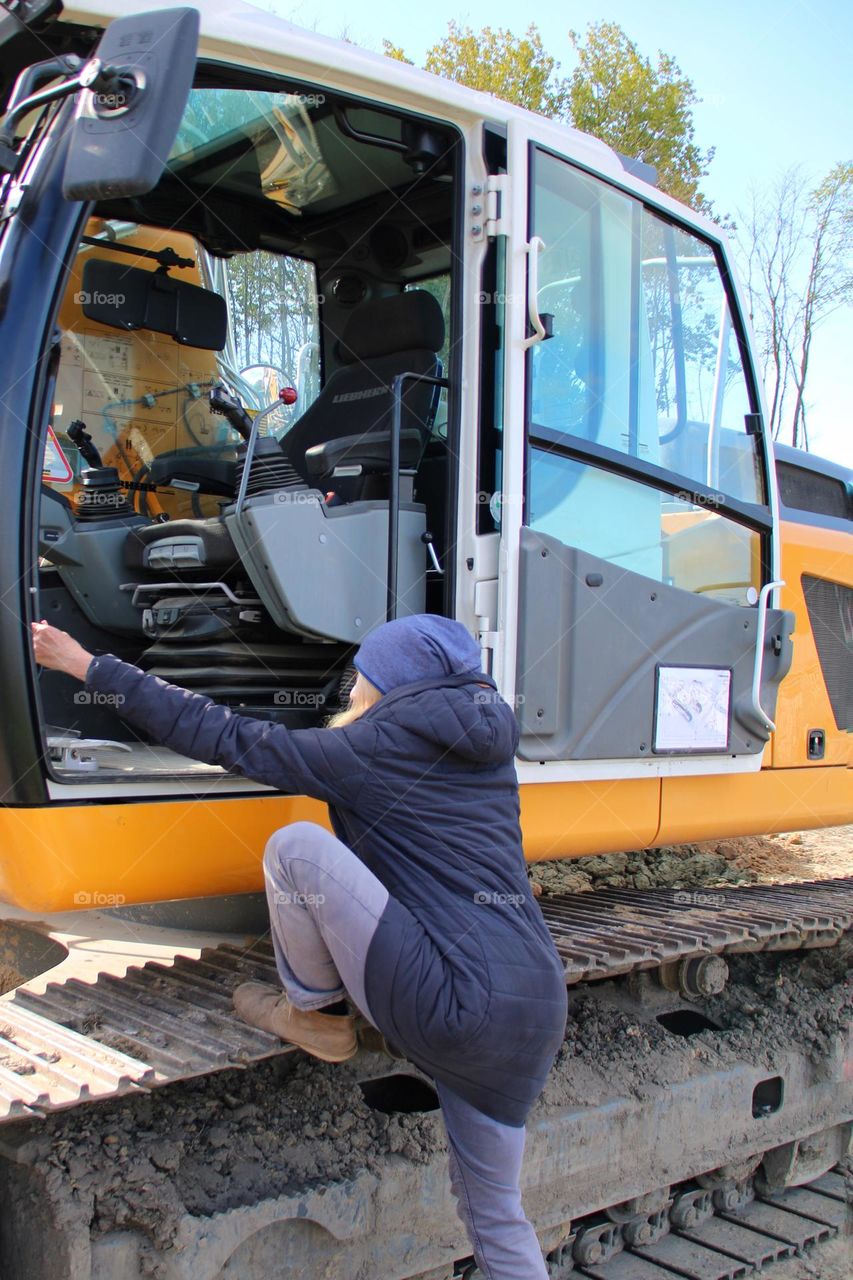 A woman climbs into the driver's cab of a crawler excavator