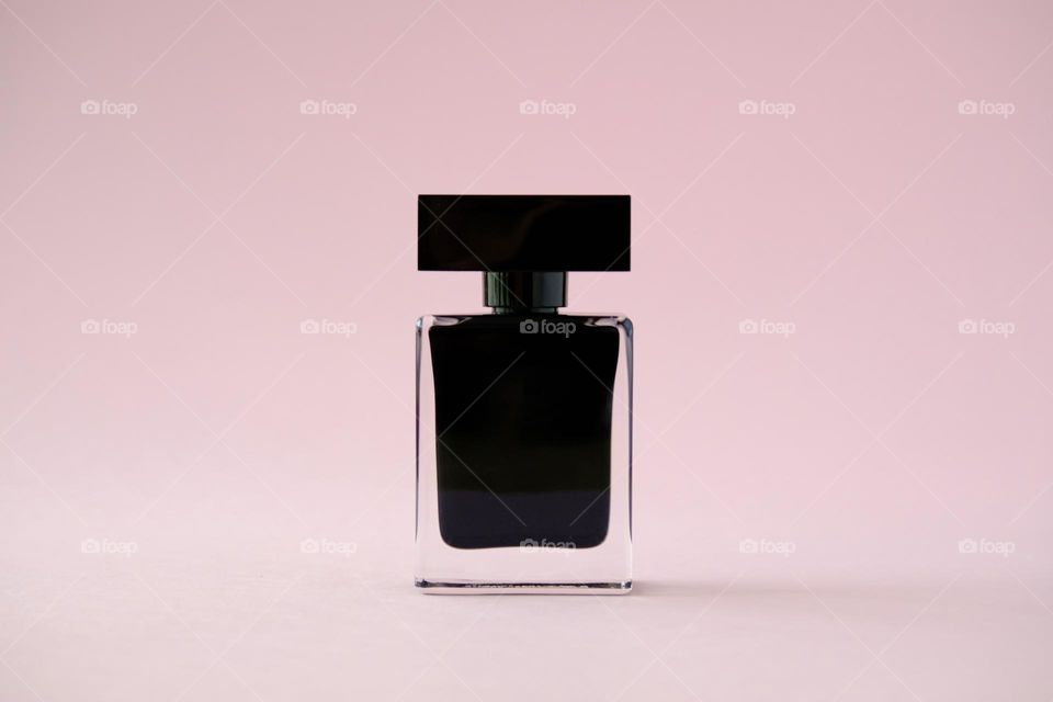 Close-up of a black perfume bottle isolated on pink background.