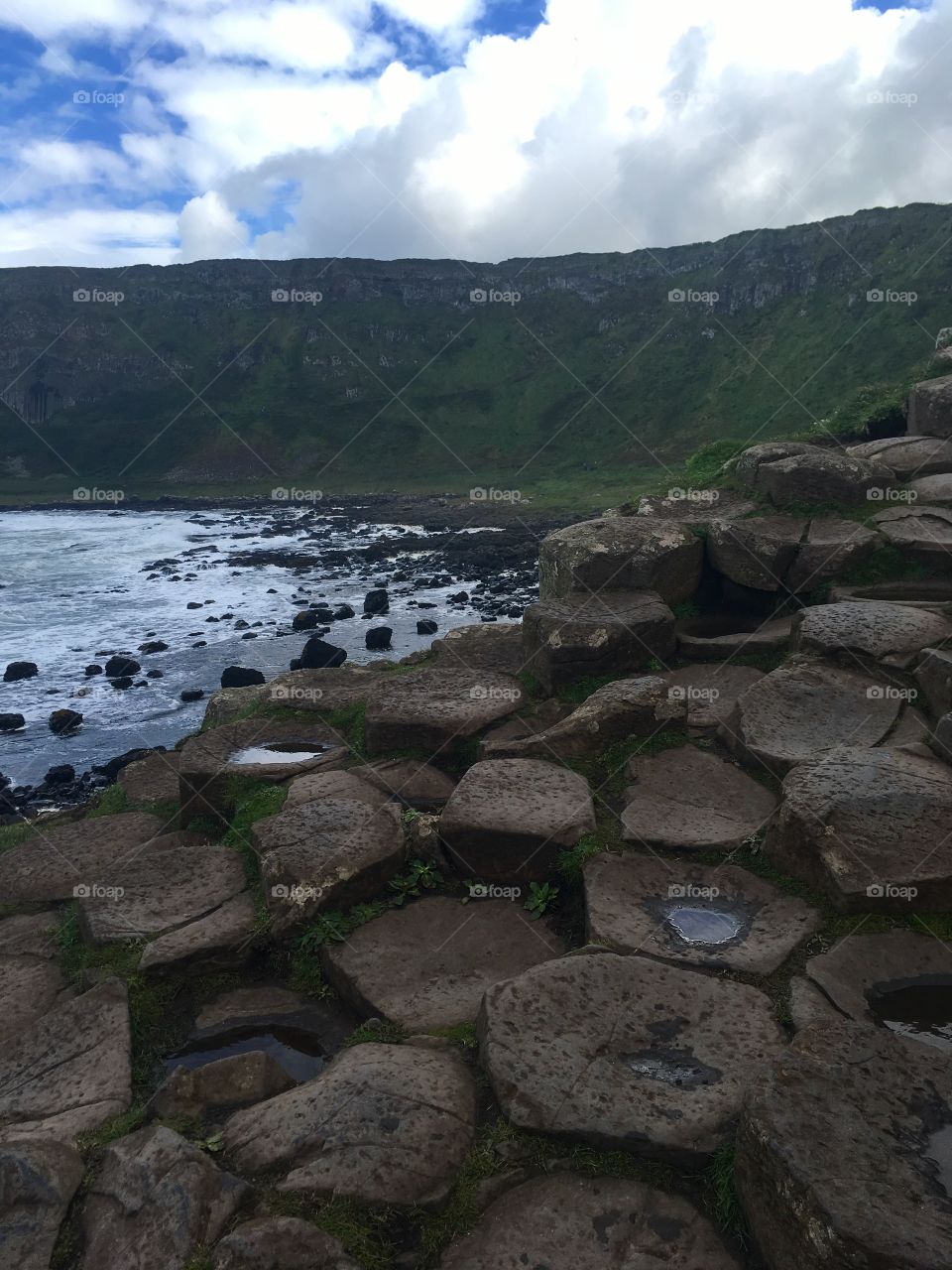 A close up view of the rocks from Giant’s Causeway in Northern Ireland with a view of the water and mountains in the distance 