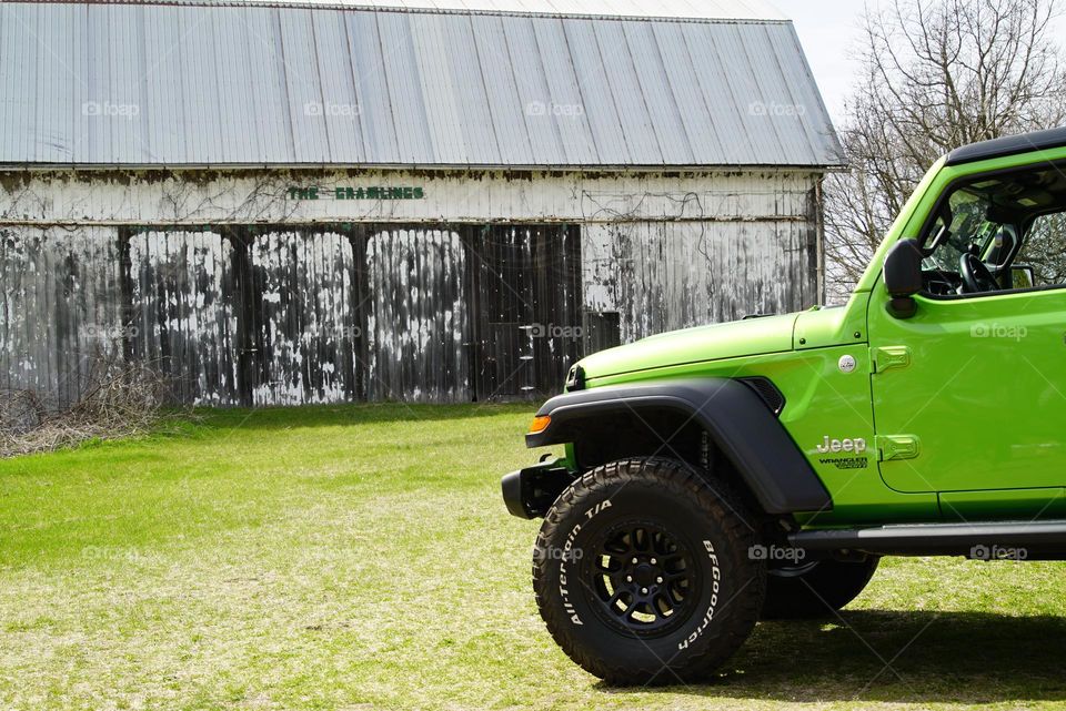Green jeep parked near an old barn