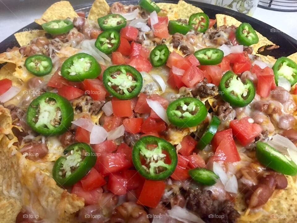 A round platter full of nachos topped with colorful diced tomatoes onions and jalapeños.