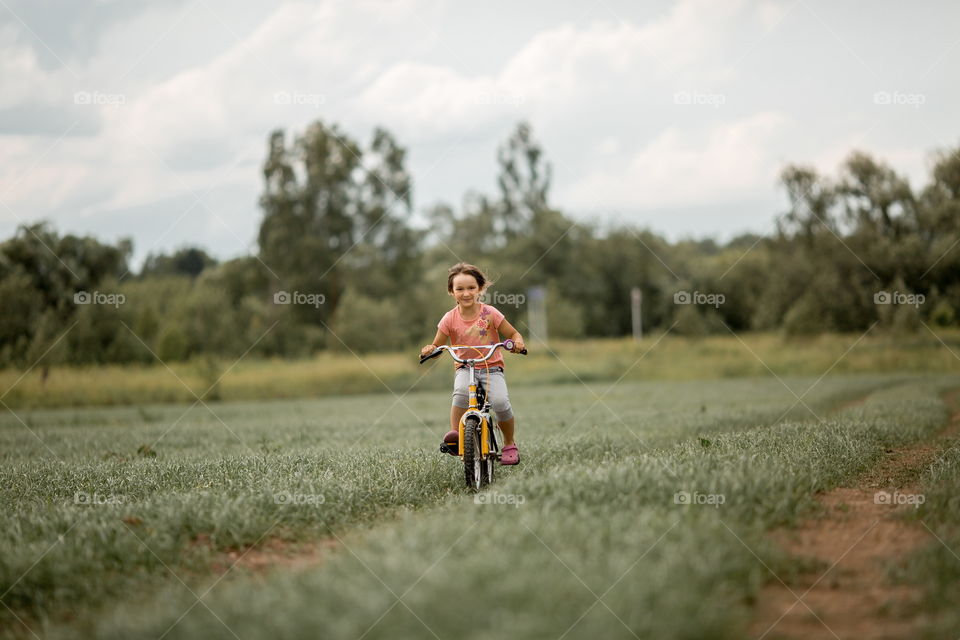 Little girl with bicycle in the summer field 