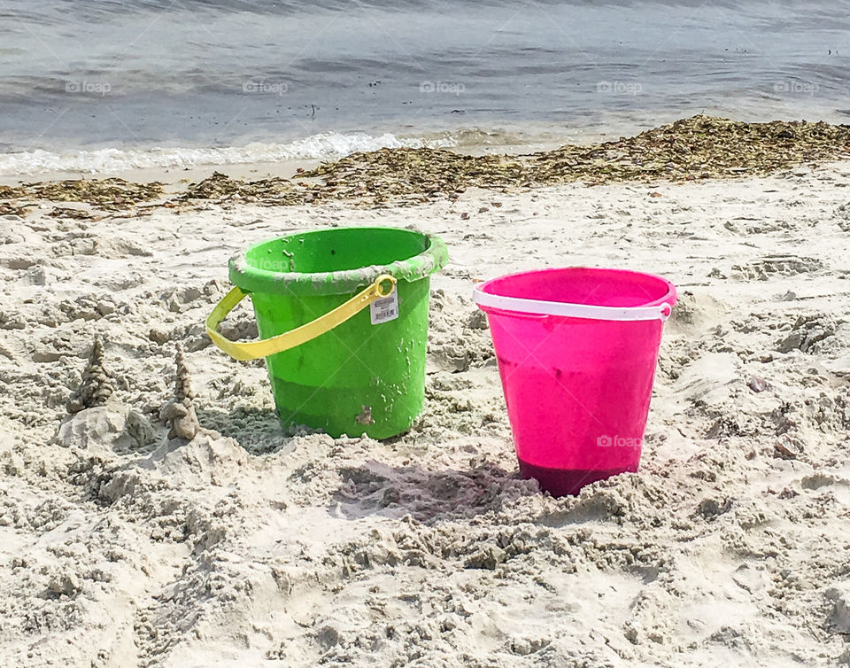 Colorful, bright sand pails at the ocean waiting to be filled and played with.  Green and pink stand out against the sand. 