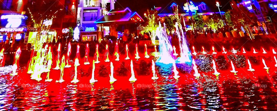 Brilliant multi colored fall of water from shooting fountain into shimmering lake at The Island in TN