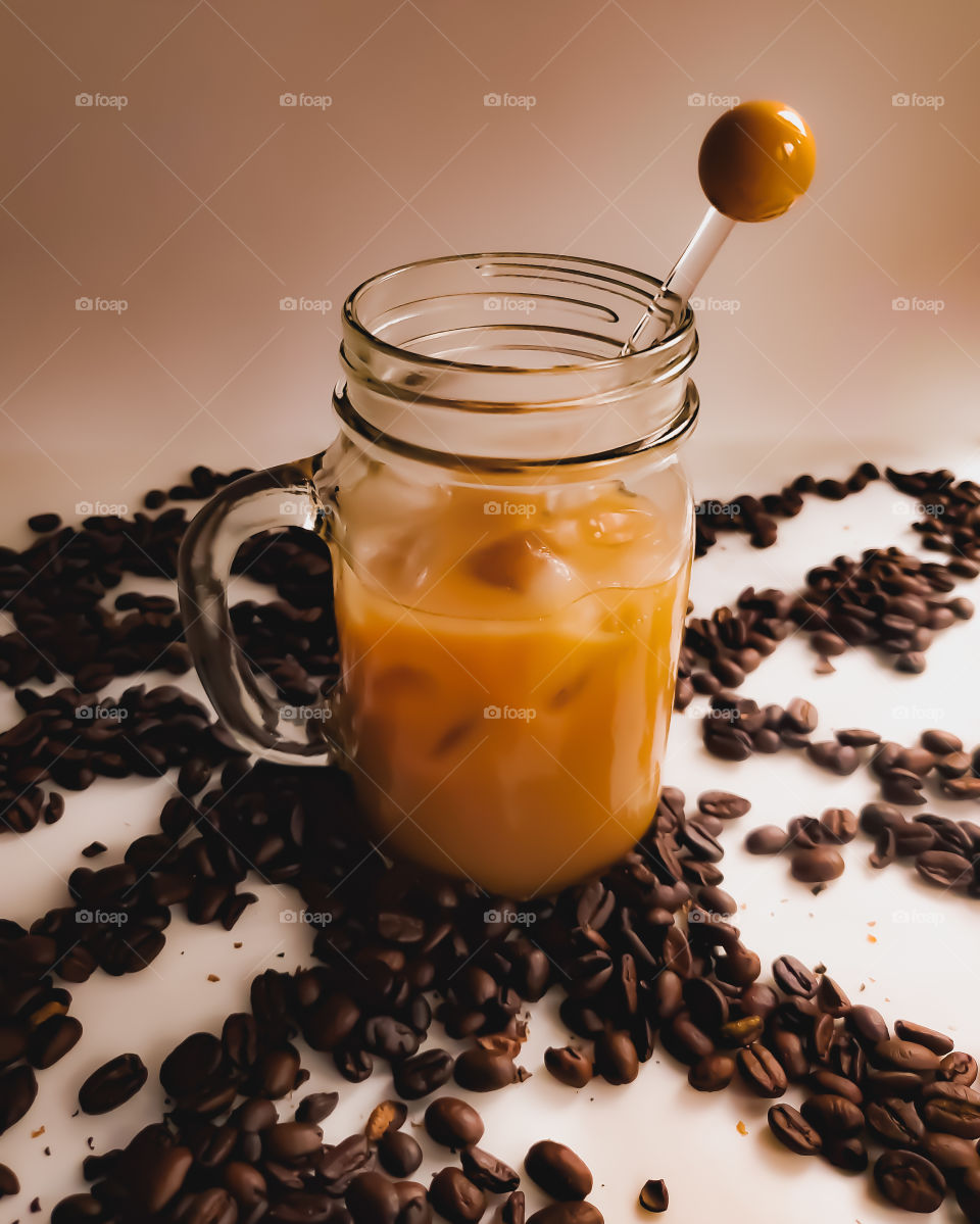 Cold brew ice coffee with creamer surrounded by whole bean coffee beans.