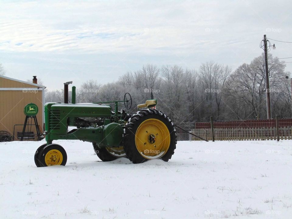 Green John Deere tractor parked in a snow covered farmyard. 