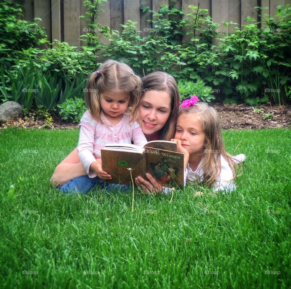 Mother and daughters in park reading story book