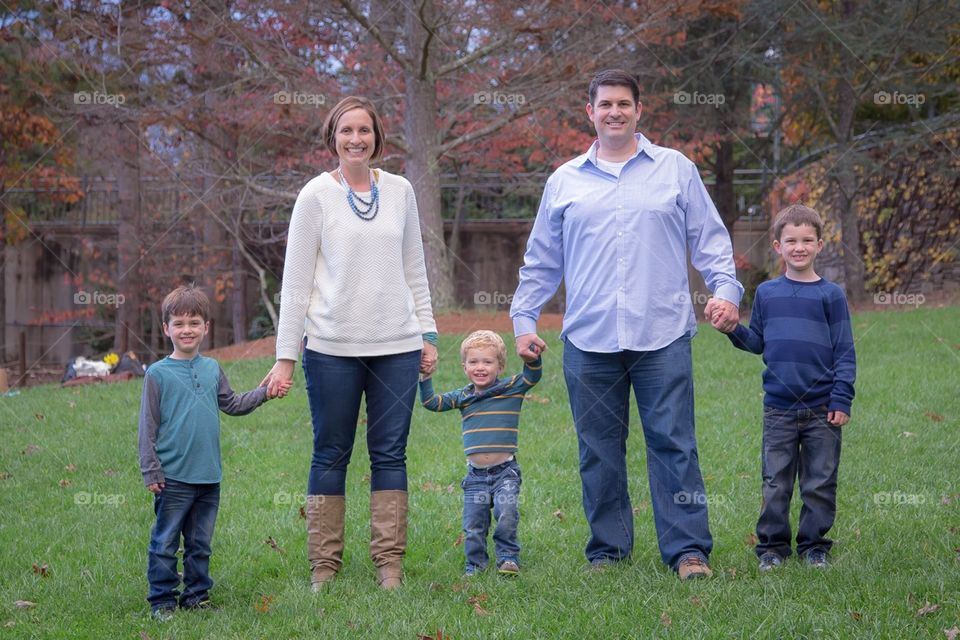 Family poses while holding hands in grass with little boys