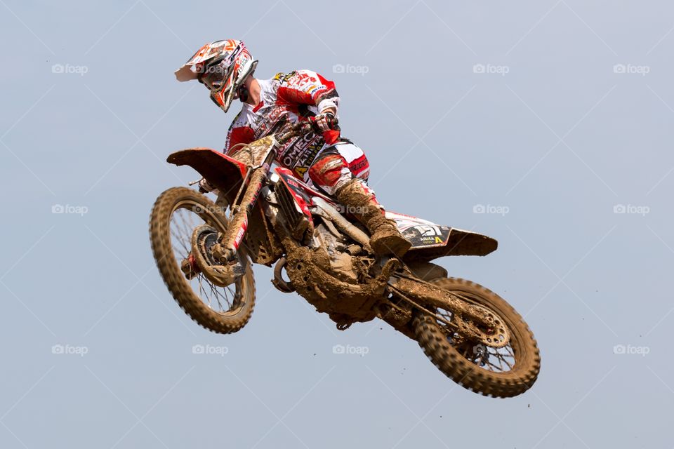 Motorcycle high up in the air. Motocross motorcycle jumps high in the air. Rider has white and red clothing. Motorcycle is dirty and covered with mud