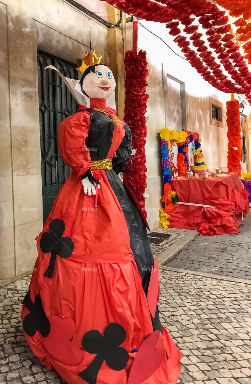 A figure of the Queen of clubs in a street decorated with paper flowers