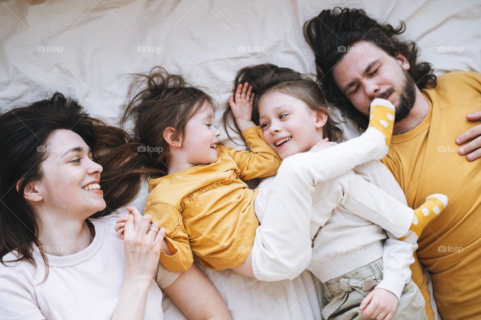 Young happy family with two children girls on bed at the cozy home, view from top