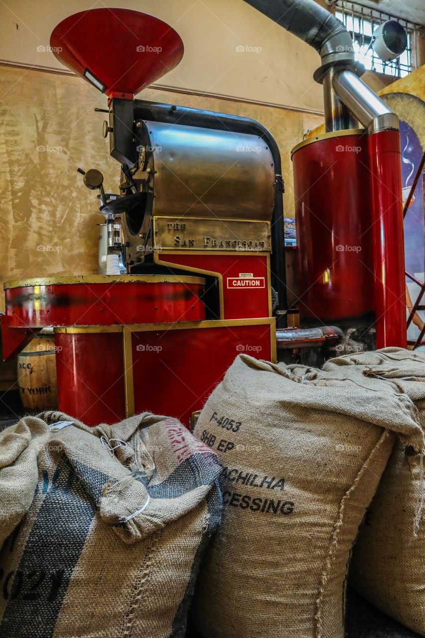 Big vintage red coffee roaster in a San Francisco coffee shop with sacks of fresh coffee beans ready to be roasted and enjoyed by customers