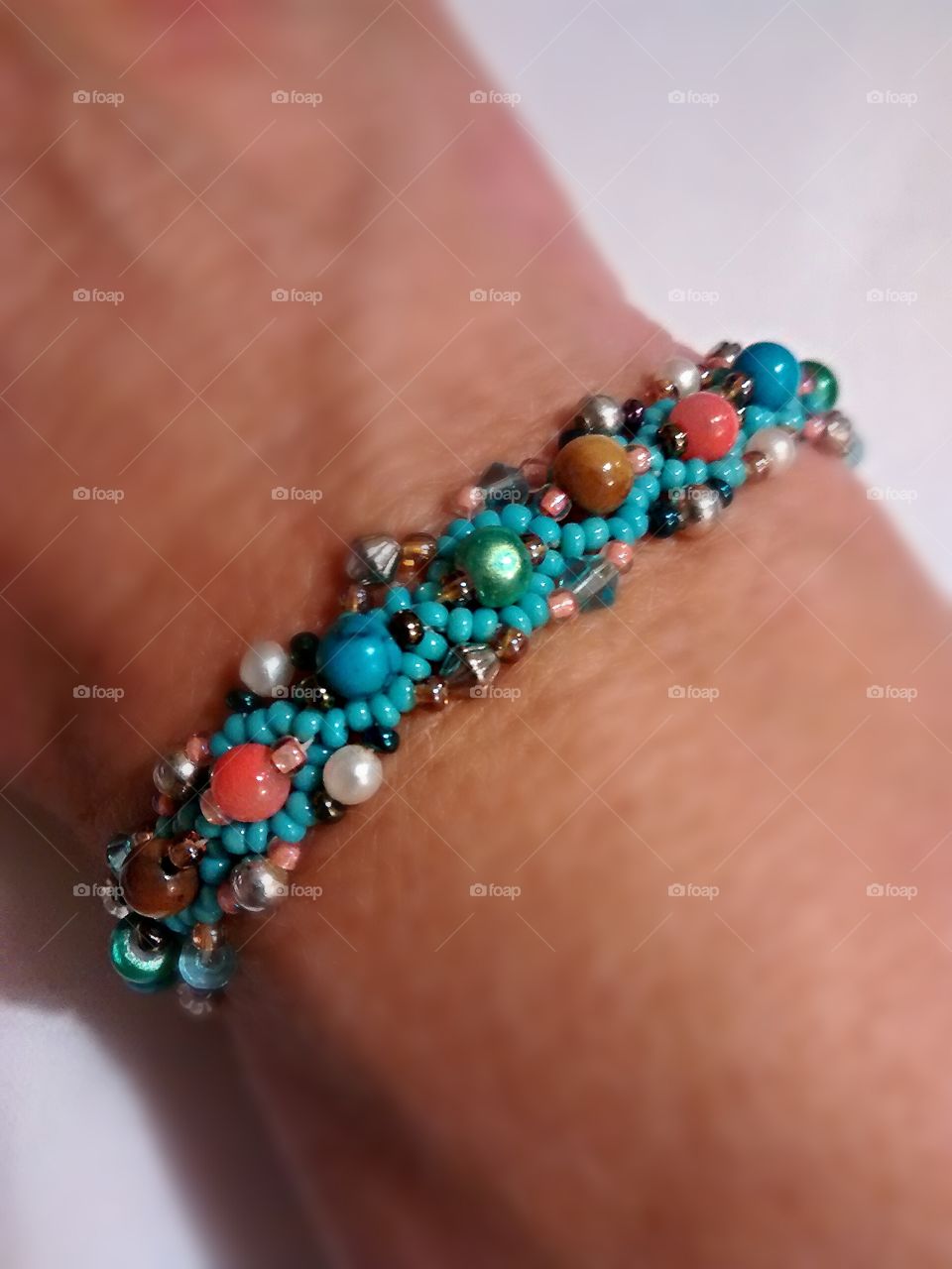 Inspired by marine colors, this single strand seed bead bracelet is embellished with multiple tiny precious stone, metal, and faux pearls.