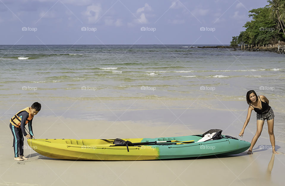 Mom and son Towing kayaks on the beach into the sea at Koh Kood, Trat in Thailand.