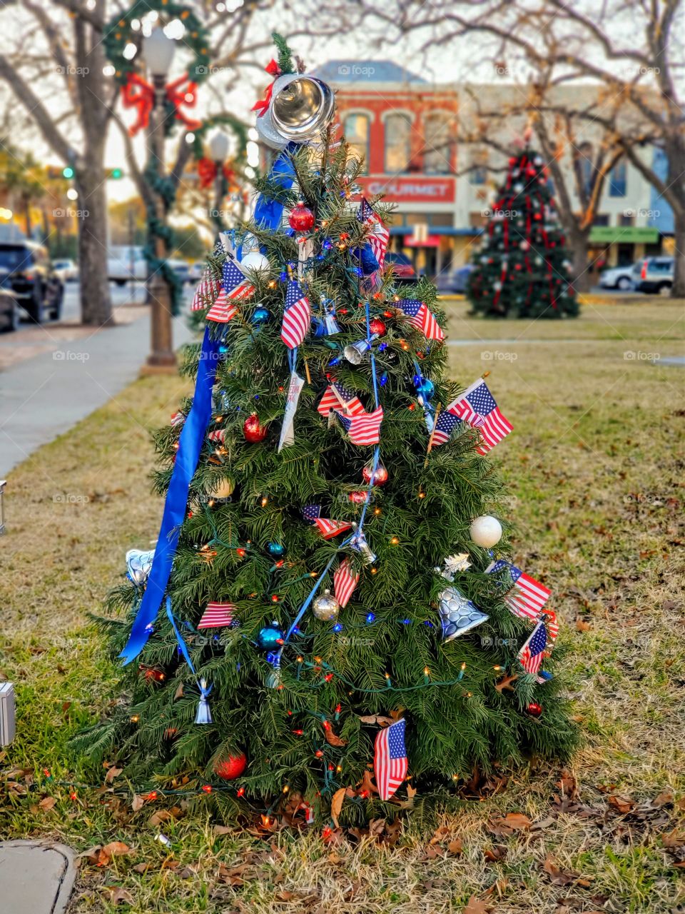 Christmas tree contest at town park. Patriotic tree pictured with another tree in the background and small town old buildings in the background.