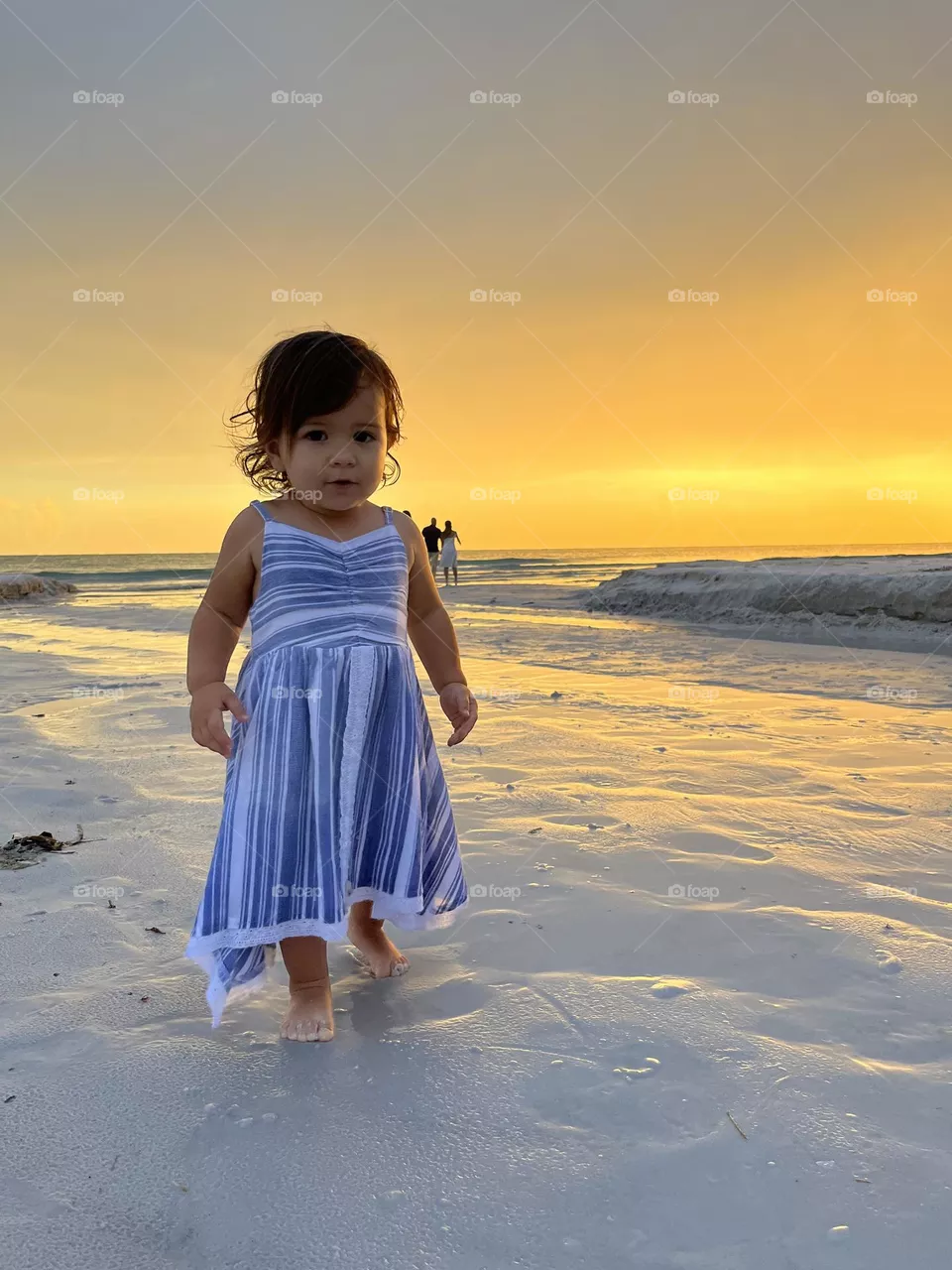 Toddler walking by the water at the beach during sunset.