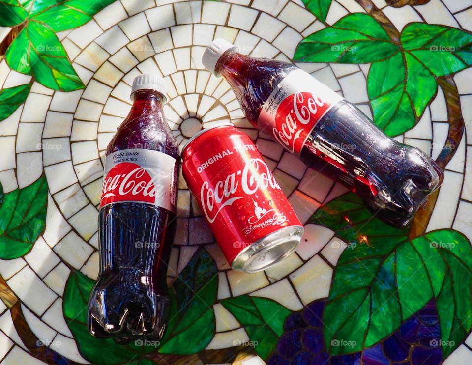 Two Diet Coke bottles and a coke can on a garden table.