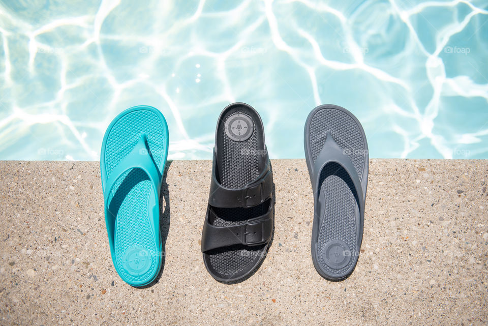 Flat lay of women's sandals on the ledge of an outdoor swimming pool