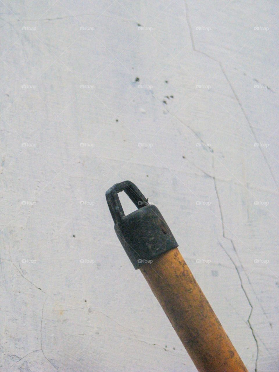 Close-up view of the tip of a stick or tool that has a black handle on a cracked white wall background