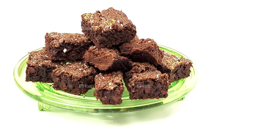 Chocolate brownies on a green glass plate with a white background 