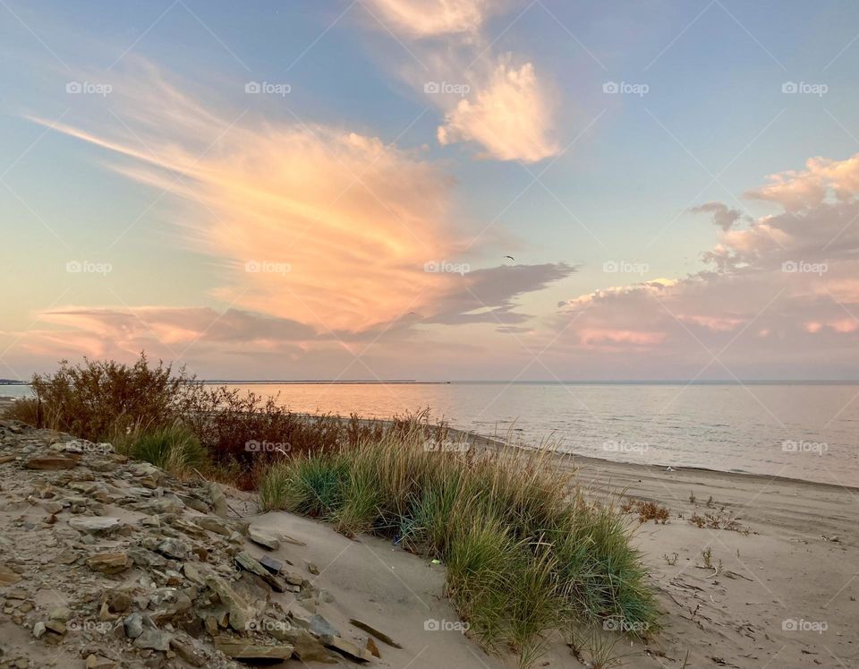 Pink and purple sunset on lake eerie shoreline on Cedar Point’s sandy, rocky beach with beach grass in foreground