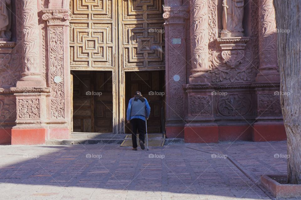 A man with a cane is about to walk through the wooden door entrance to a church in San Miguel de Allende.