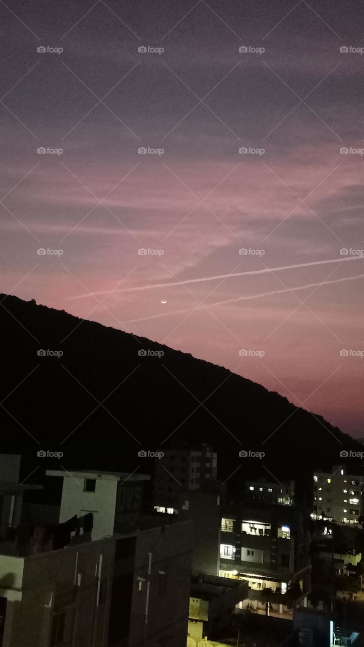 jet contrails crossing the half moon at colourful evening