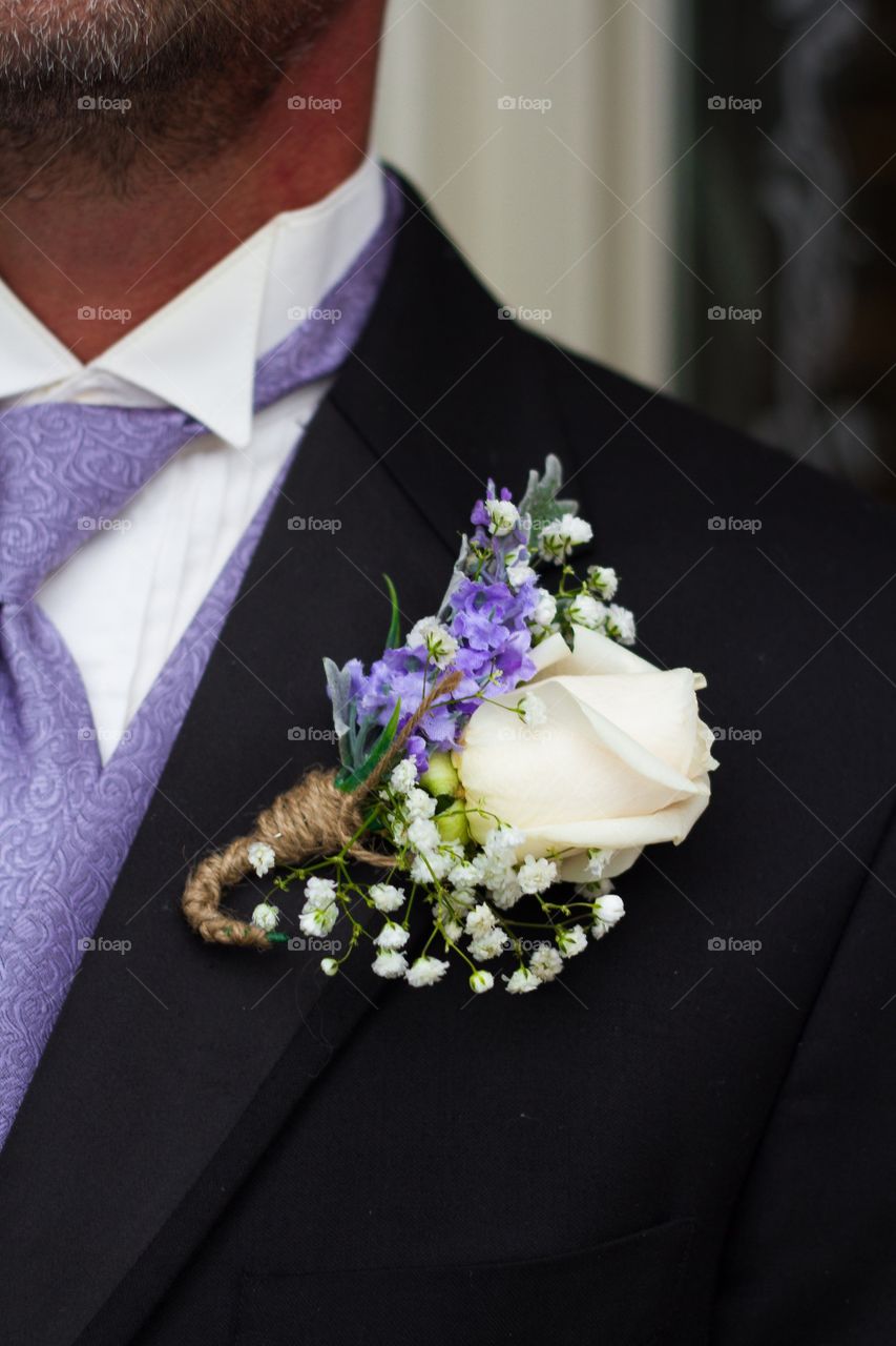 Groom's boutonnière on his lapel with a white rose, baby's breath and lavender, wrapped in twine