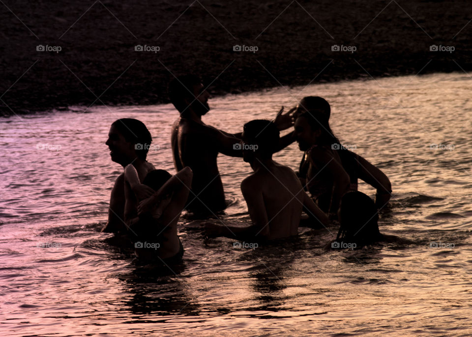 Young people having fun in the river, they are silhouetted against the water