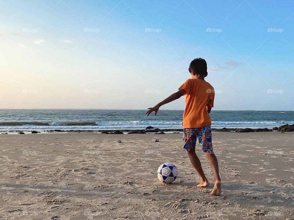 Boy playing football at the beach 