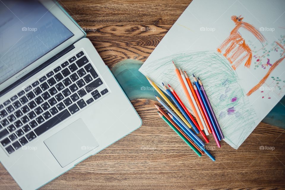 Children drawing with colorful pencils and laptop at wooden desk indoor