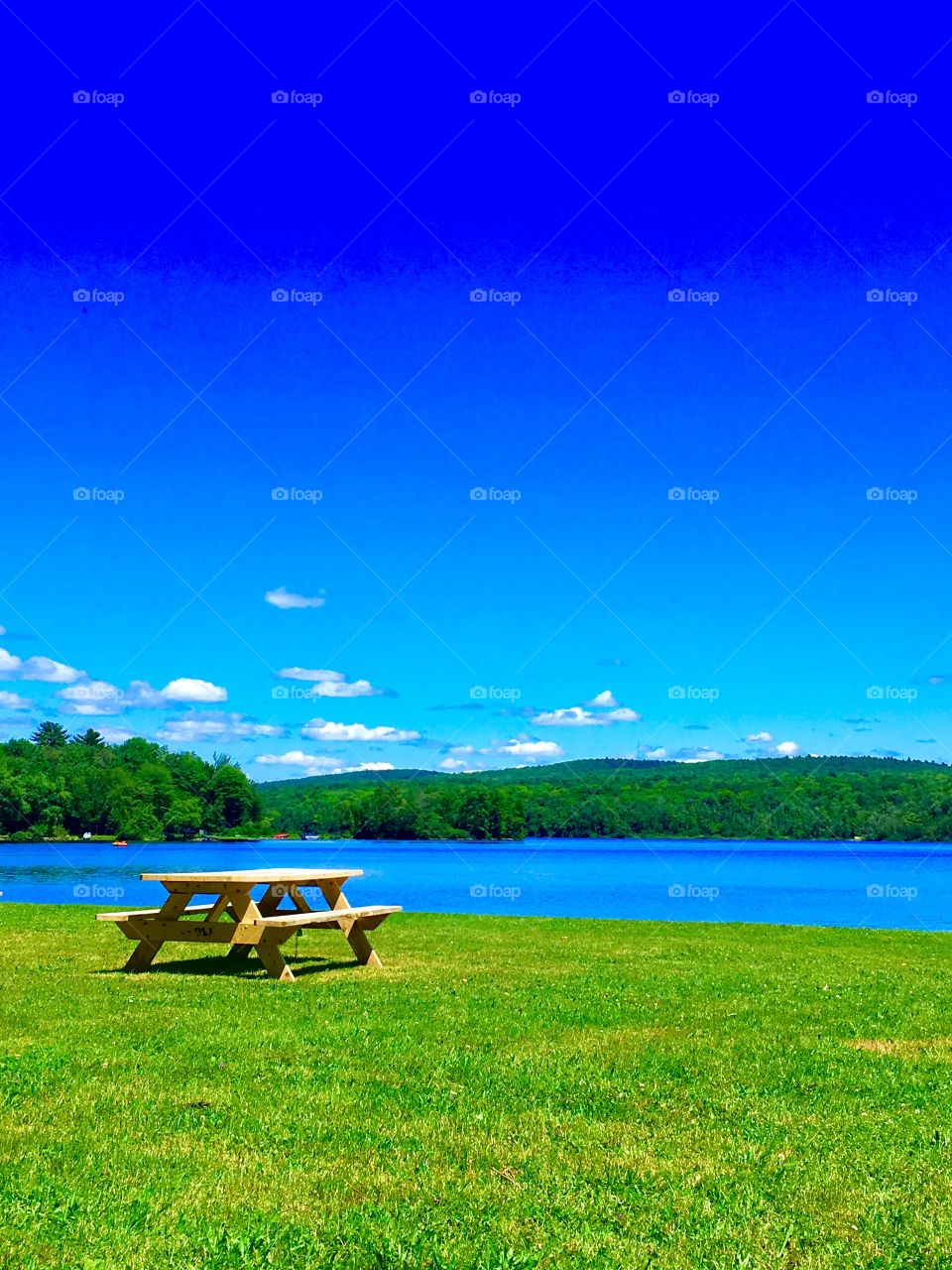A clear blue sky on a sunny summers day with a picnic table overlooking a lake in Maine.
