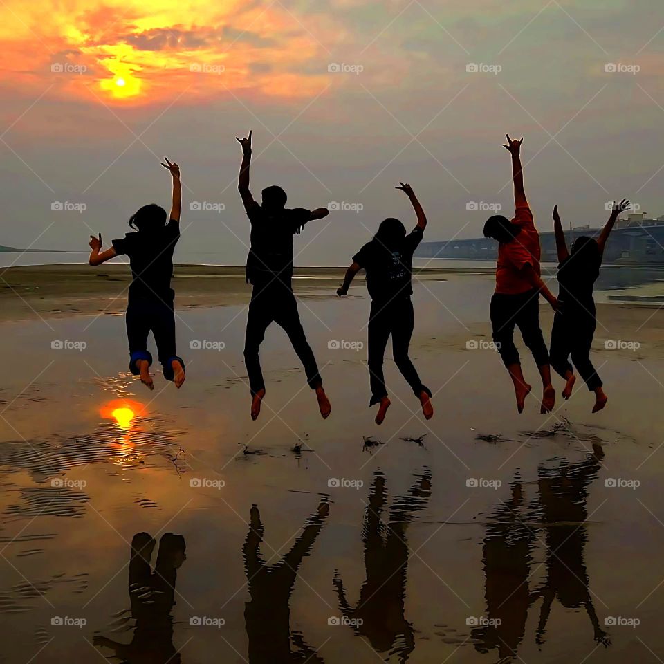 The image conveys a sense of freedom, energy, and the carefree spirit of youth, set against the serene backdrop of the ocean and horizon. The overall mood is one of happiness and togetherness, celebrating the simple pleasures of life.