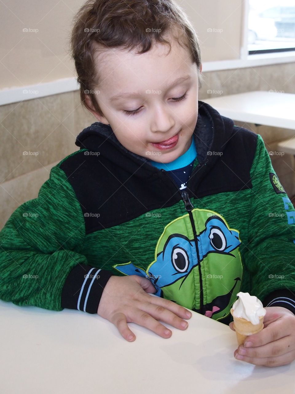 A little boy really enjoys his small vanilla cone that really hits the spot. 
