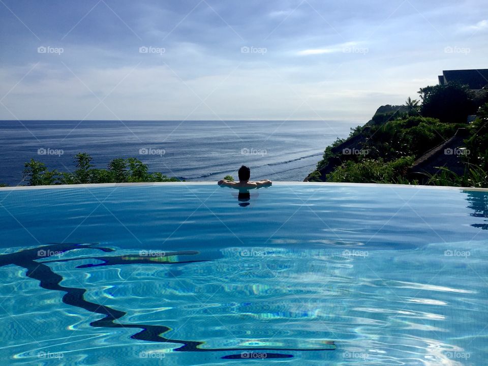Man looking at the ocean from an above the valley swimming pool at a resort in Badung, Bali, Indonesia 