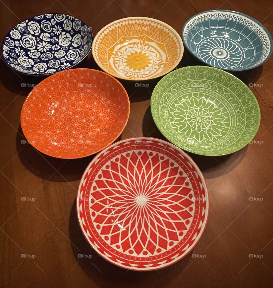 Six colorful bowls arranged with one bowl in front and the others behind it in a triangular shape. Each bowl has a unique design adding to their visual charm. The bright, bold colors and diverse patterns create a lively and dynamic display.