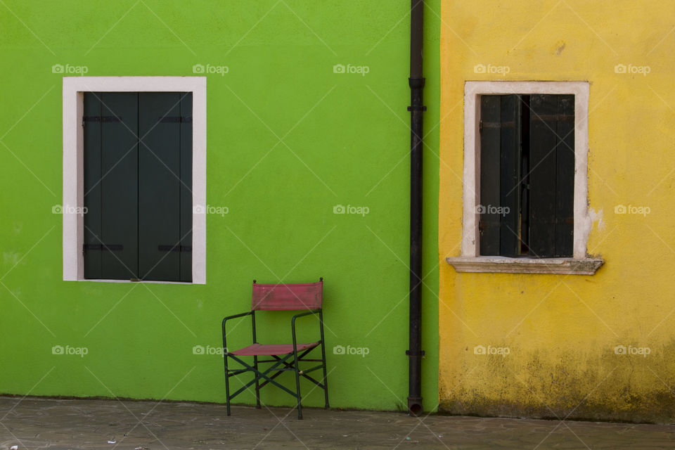 Chair in front of a green and yellow house in a street of Burano. 