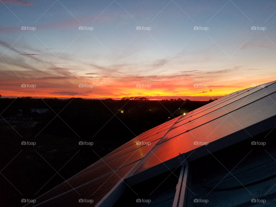 Vibrant colorful sunset light reflects off solar panels on top of roof