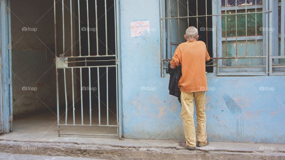 A back view of an elderly man facing a barred window in Havana, Cuba b