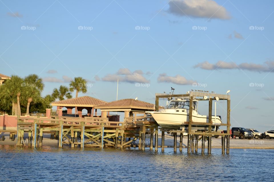 A wooden boat dock with two wooden coverings on posts and a boat elevated at the end on a river